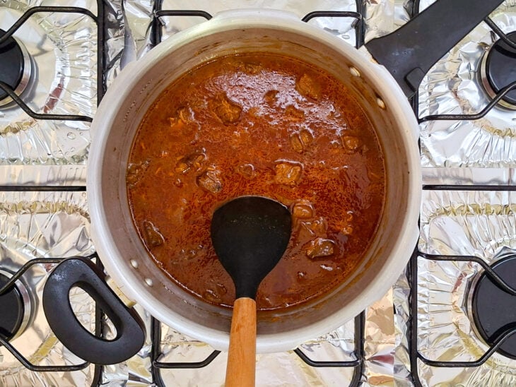 Água quente sendo vertida de uma chaleira para dentro da panela de pressão até cobrir a carne.