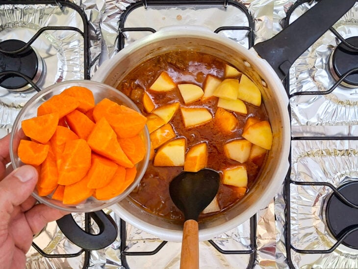 Pedaços médios de batata e cenoura cruas sendo adicionados à panela aberta com a carne cozida.