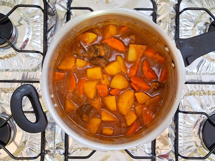 Colher misturando os legumes ao molho encorpado e avermelhado com a carne de panela.