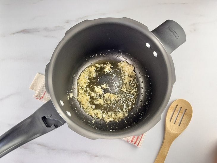 Uma panela de pressão refogando cebola e alho.