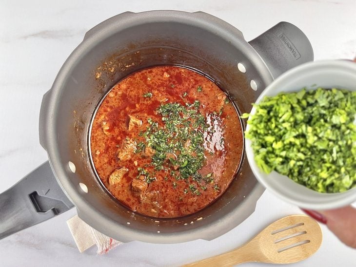 Uma panela contendo carne, molho e água, cheiro-verde.