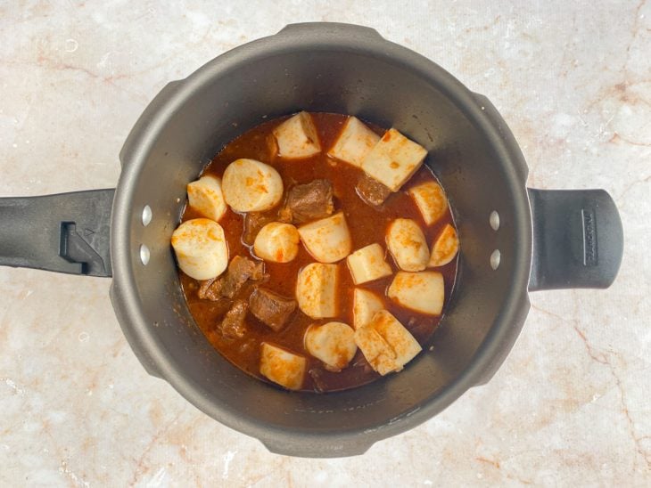 Uma panela de pressão com a carne, o molho e a mandioca.
