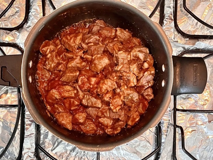 Panela com carne e molho avermelhado.