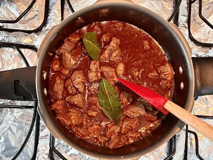 Panela com carne, molho avermelhado e folhas verdes.