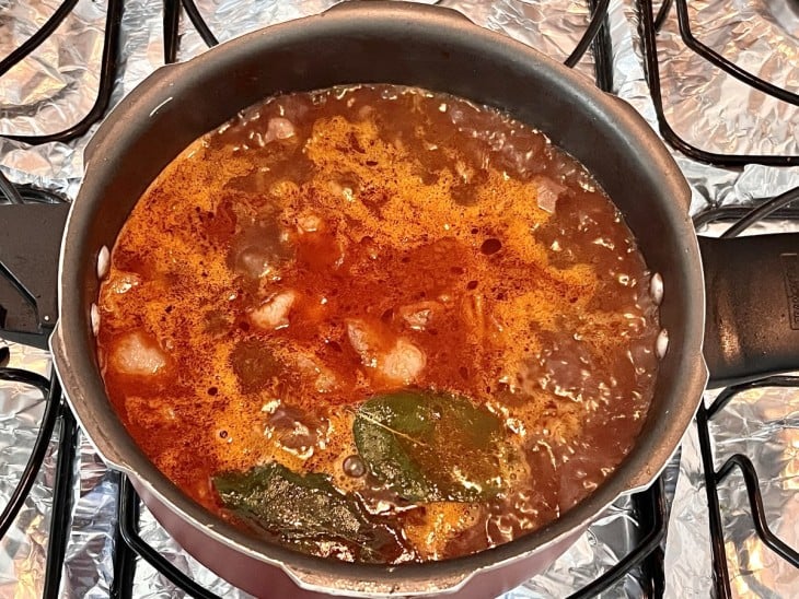 Panela com carne e molho avermelhado borbulhando.