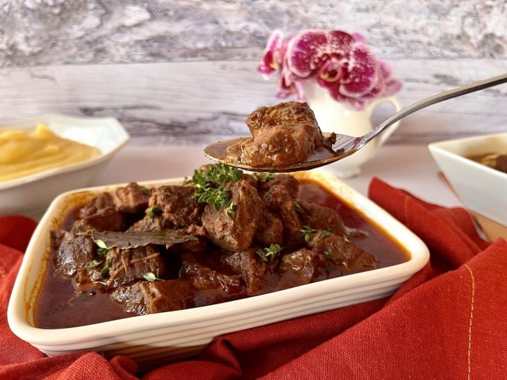 Carne de panela com vinho tinto servida em refratário branco.