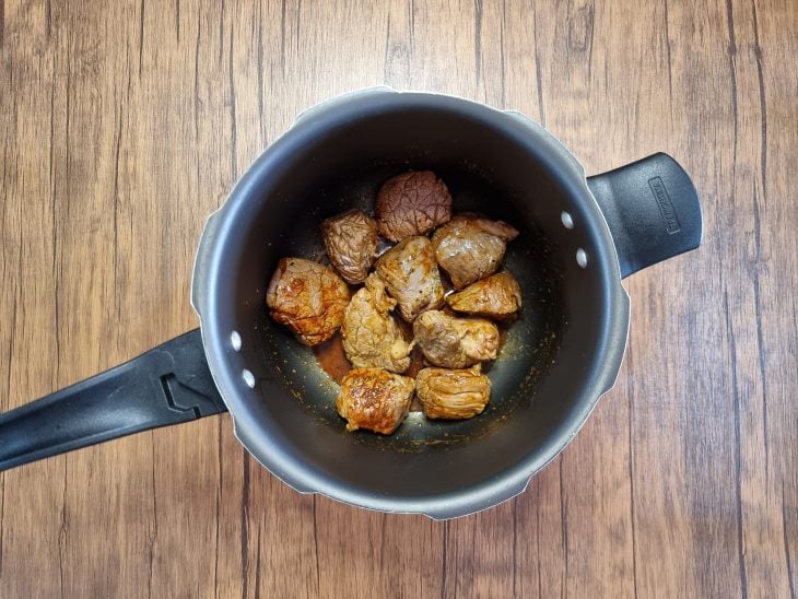 Pedaços de carne com temperos na panela.