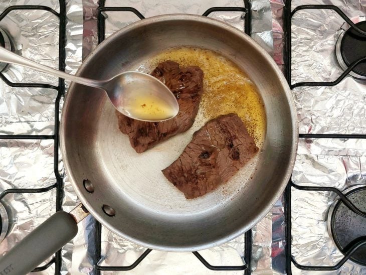 Uma frigideira fritando pedaços de carne com manteiga de garrafa.