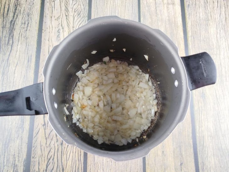 Alho e cebola refogando no óleo na panela de pressão.