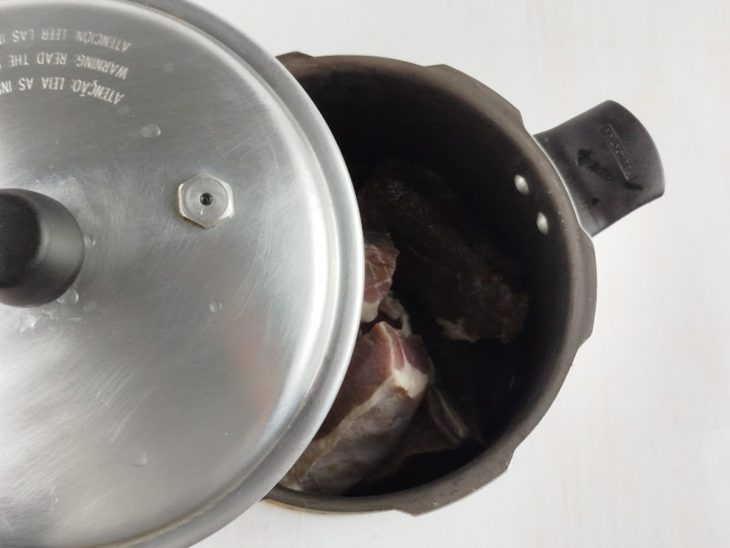 Pedaços de carne dentro da panela de pressão com água.