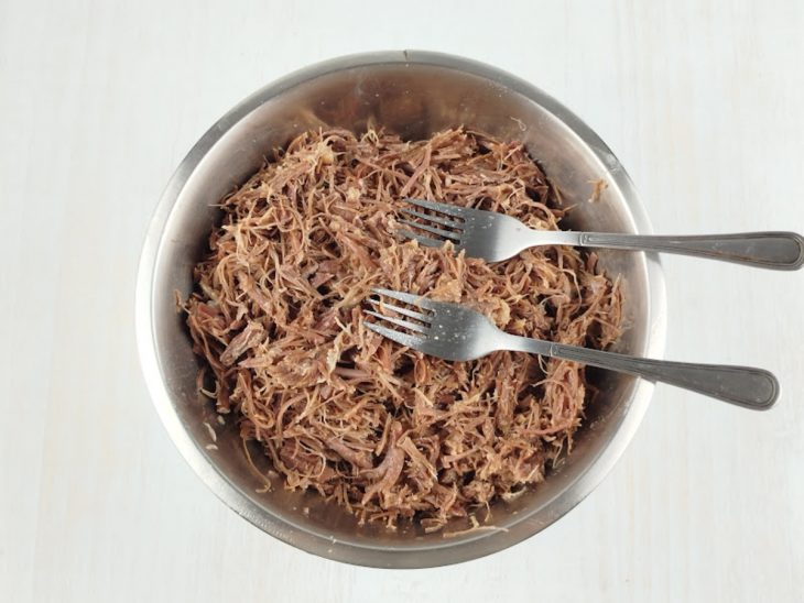 Carne cozida sendo desfiada com dois garfos.