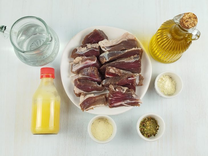 Carne de sol sendo temperada em uma tigela com azeite, água e especiarias.