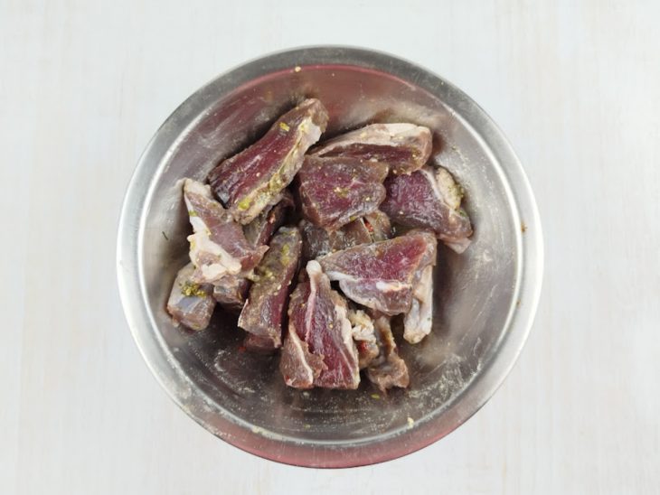 Carne de sol sendo temperada em uma tigela com azeite, água e especiarias.