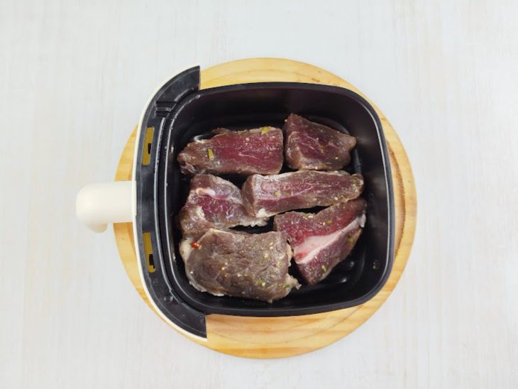 Carne temperada disposta na cesta da air fryer.
