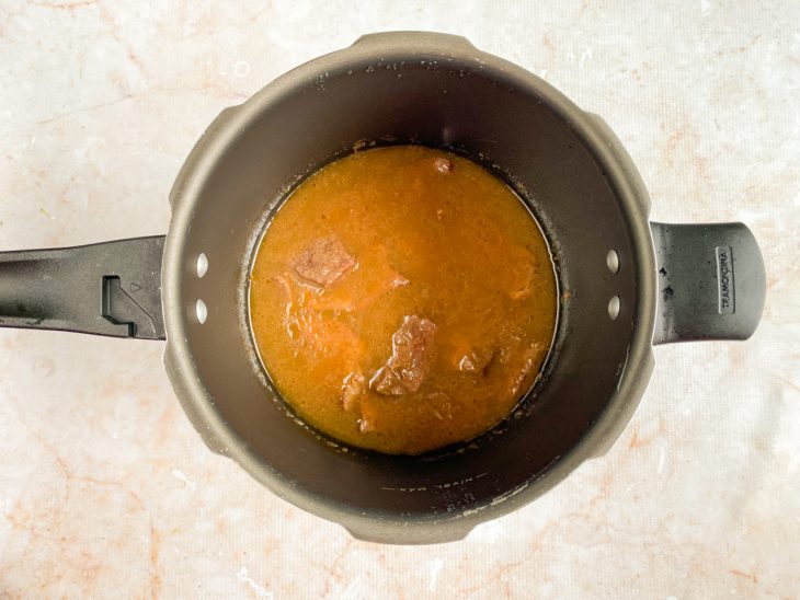 Caldo despejado na panela com carne selada.