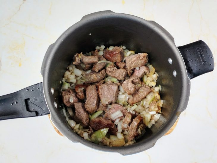 Carne e cebola refogando na panela de pressão com azeite.