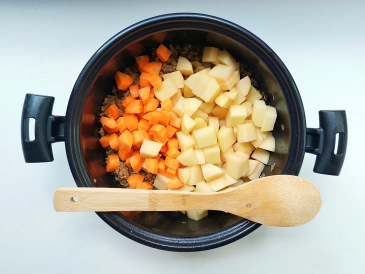 Batatas e cenouras picadas adicionadas a panela com carne moída.