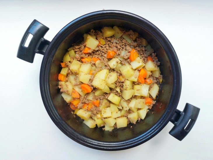 Carne moída com batatas e cenouras em uma panela.