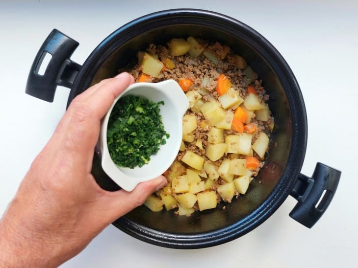 Cheiro-verde sendo adicionado a carne moída com legumes.