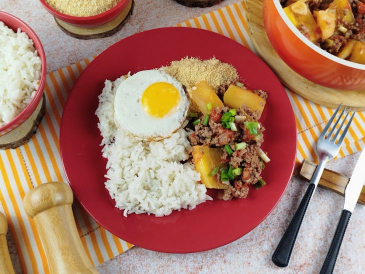 Carne moída com mandioca servida com arroz e ovo num prato individual.