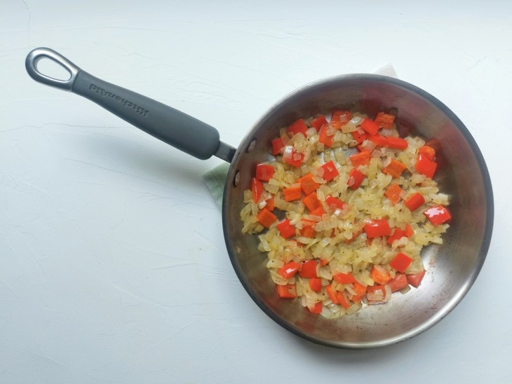 Uma frigideira contendo cebola e pimentão refogados.