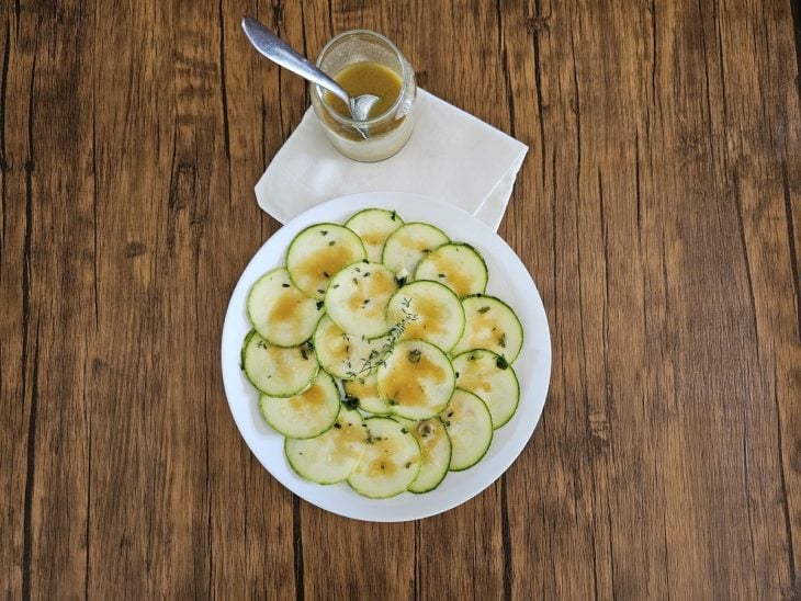 Um prato contendo carpaccio de abobrinha com molho de mostarda.