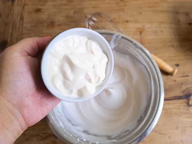 Creme de leite sendo adicionado à tigela com claras e açúcar.