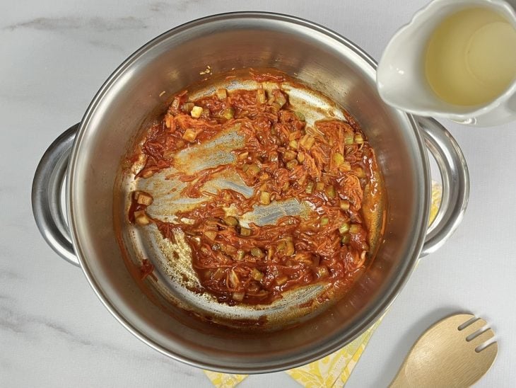 Uma panela com extrato de tomate, cenoura, vinho e temperos refogando.