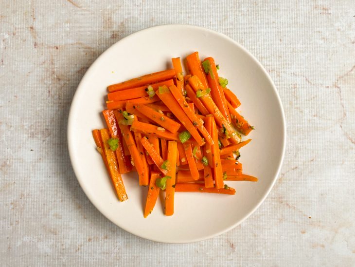 Cenouras finalizadas, e servidas em prato branco com cebolinha.