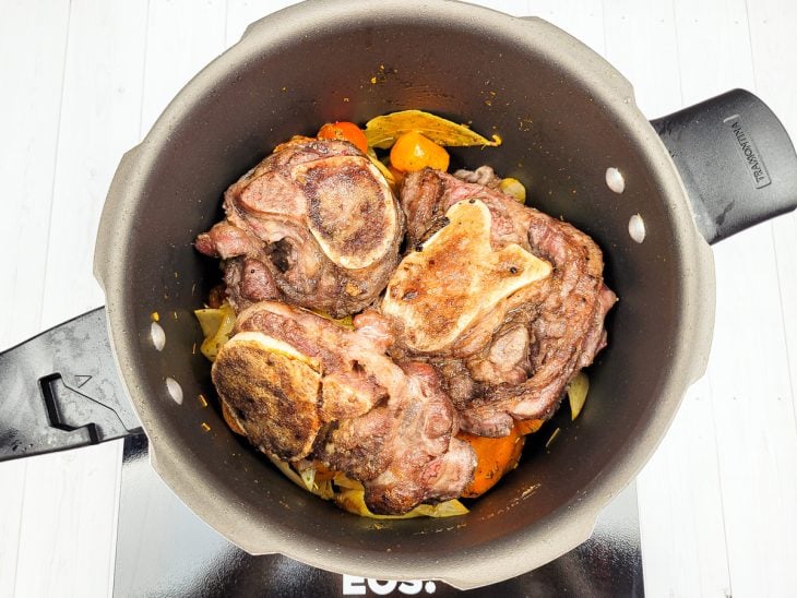 Uma panela com ossobuco e legumes em processo de cozimento.