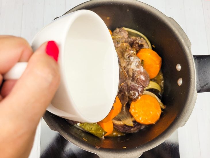 Uma panela com ossobuco, legumes, pimenta-do-reino, vinho e água em processo de cozimento.