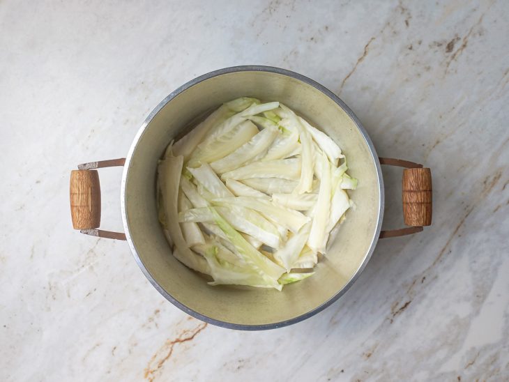 Fundo da panela sendo forrado com os talos retirados das folhas.