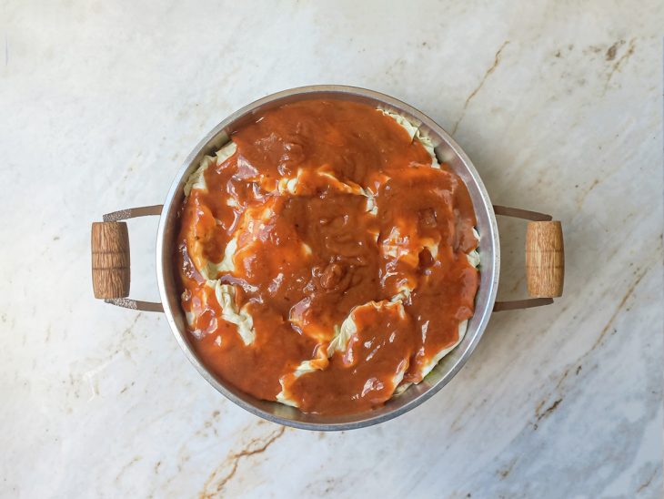 Folhas cobrindo os charutos e molho de tomate sendo despejado por cima.