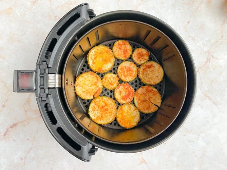Cesta de air fryer com as fatias de abobrinha.