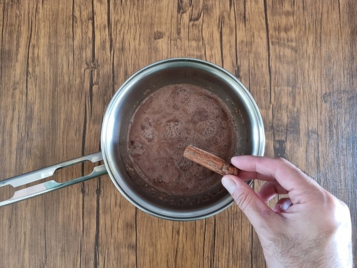 Canela em pau sendo adicionada na panela com o chocolate cremoso.