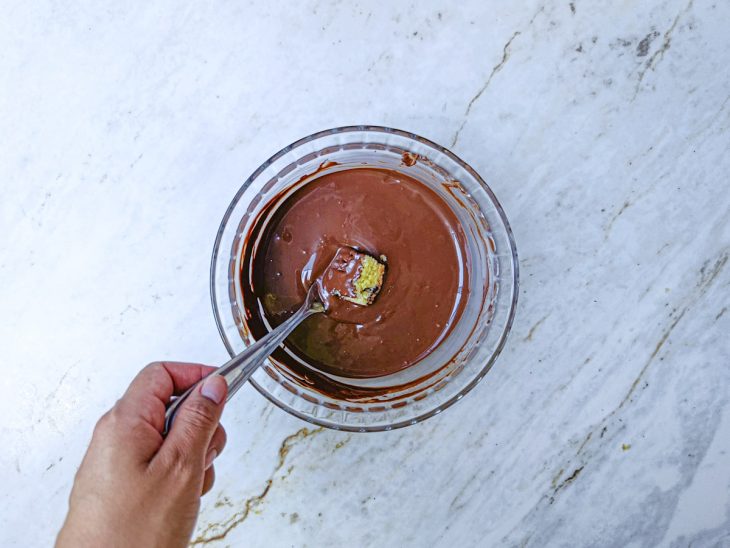 Com auxílio de um garfo, cubos do chocotone mergulhados no chocolate.