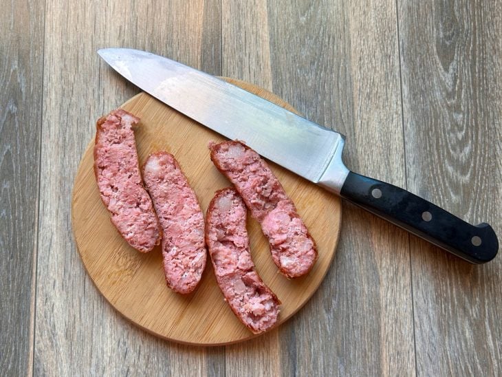 Gomos de linguiça grelhados cortados ao meio sobre uma tábua redonda de madeira.