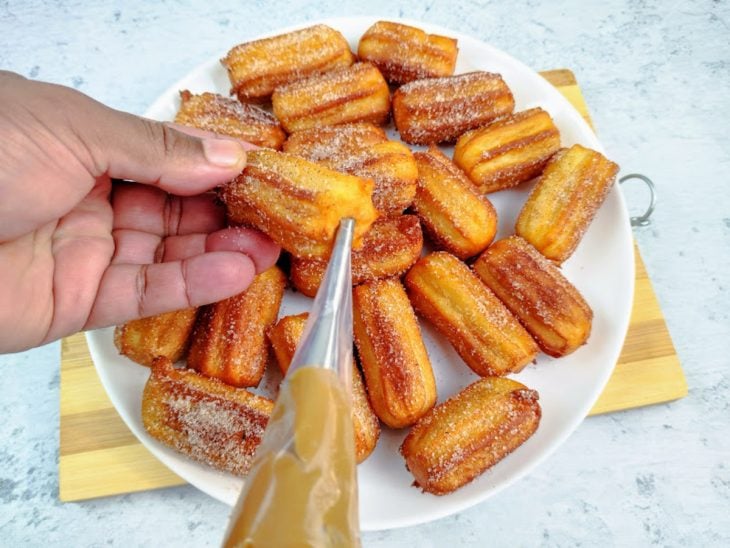 Um prato com churros sendo recheado.