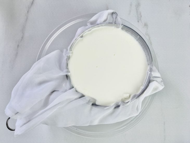 Conteúdo da panela colocado em uma peneira coberta por pano.