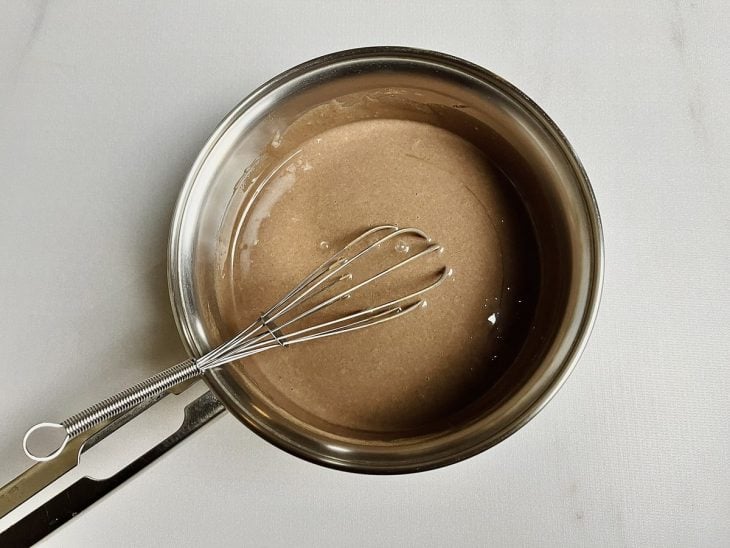 Leite condensado e chocolate em pó incorporados em uma panela com auxílio de um fouet (batedor de arame).