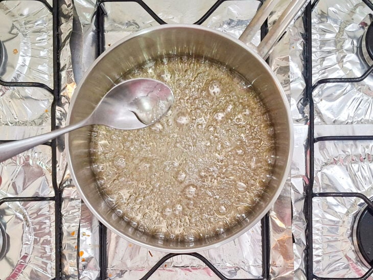 Água e açúcar sendo cozidos em uma panela até formar uma calda espessa.