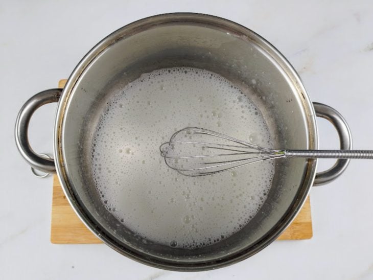 Uma panela com leite de coco, claras e adoçante, e um fouet para misturar.