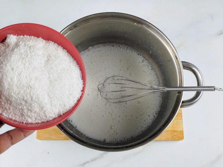Coco ralado sendo agregado à panela com os outros ingredientes.