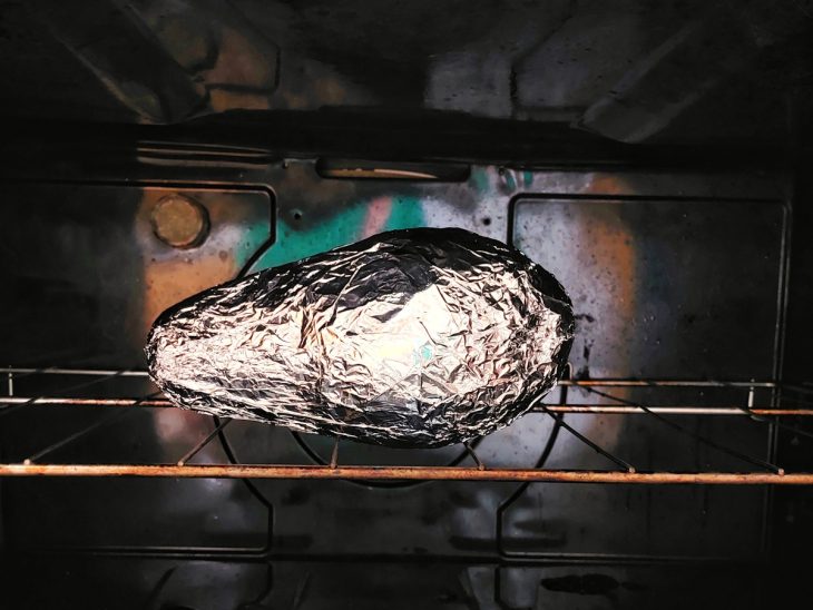 Um forno contendo um abacate embrulhado com papel alumínio.