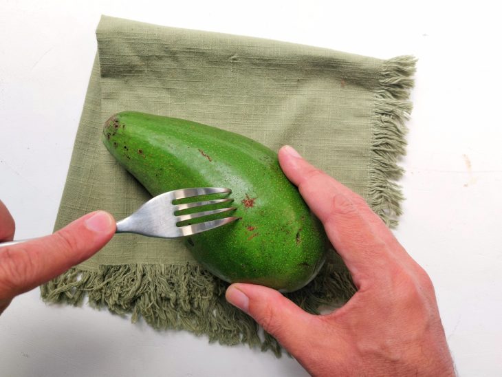 Um abacate sendo perfurado com garfo.