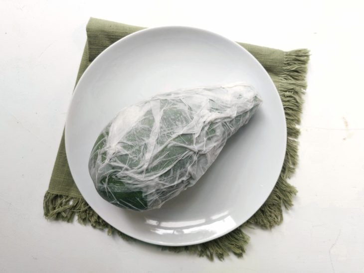 Um prato contendo um abacate embrulhado em papel toalha umedecida.
