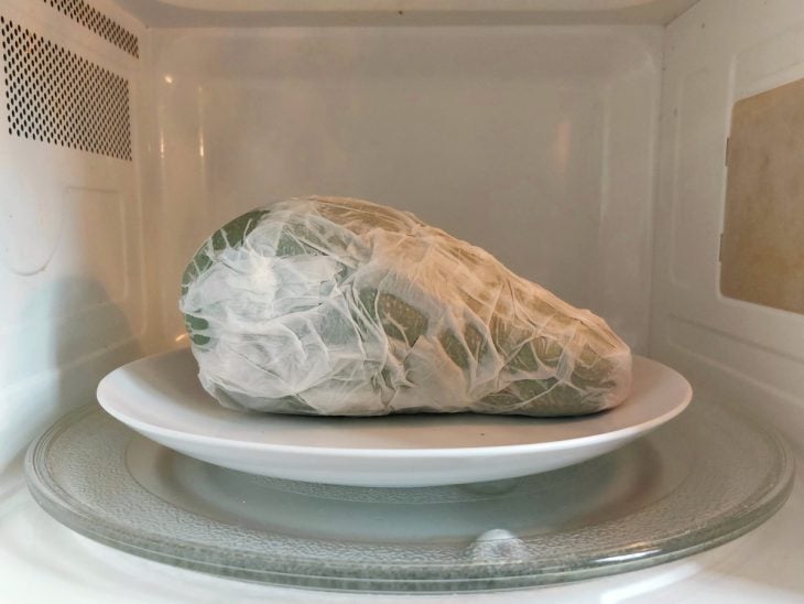 Um micro-ondas com um prato contendo um abacate embrulhado em papel toalha umedecida.