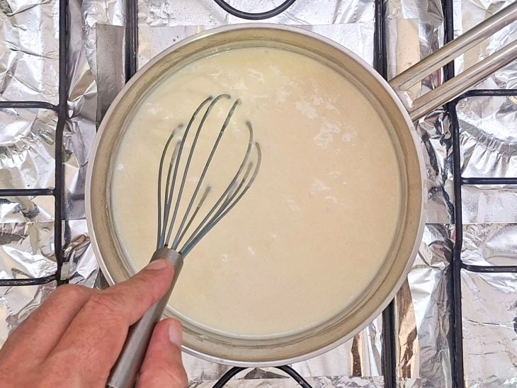 Molho branco recebendo creme de leite e queijo parmesão ralado.