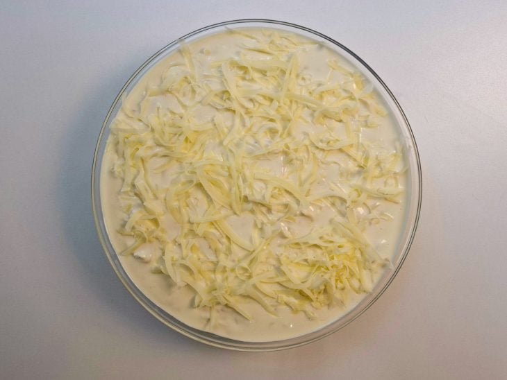 Massa coberta com molho branco e queijo antes de gratinar.