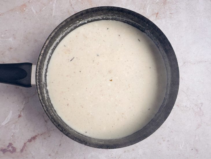 Molho branco pronto e encorpado sendo temperado na panela.